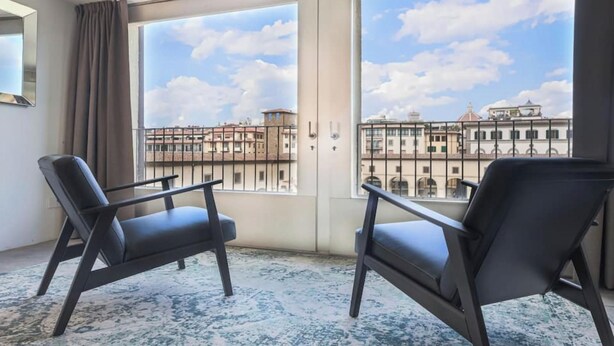 Ein Zimmer mit zwei schwarzen Stühlen, einem großen Fenster und Blick auf die Stadt sowie einem gemusterten Boden.