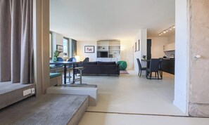 Ein modernes Wohnzimmer mit einer Couch, einem Esstisch und Stühlen. Es gibt eine Küchenzeile mit Schränken und einer Arbeitsplatte.