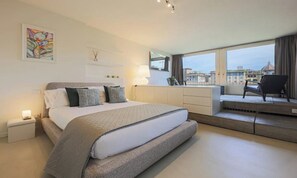 A modern bedroom with a large bed, bedside tables, a dresser, and a view of the city through large windows. - VASARI LUXURY – SOPHISTICATED FLORENCE HOME WITH RIVER VIEWS (Firenze)