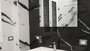 Ein modernes Badezimmer mit einem großen, weißen Waschbecken, einem Spiegel und schwarzen Marmorwänden.