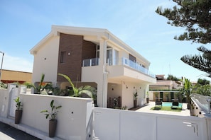 A modern two-story house with a balcony, a swimming pool, and potted plants. - Vrbo Property (Lido Manfria)
