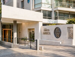 Ein modernes Gebäude mit einem markanten Eingang, einer Schrifttafel mit der Aufschrift 'Edificio America 30 La Gloria 34' und einer Treppe, die zum Eingang führt.