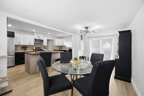 Una cocina moderna con armarios blancos, una isla central y una zona de comedor con una mesa de vidrio y sillas negras.