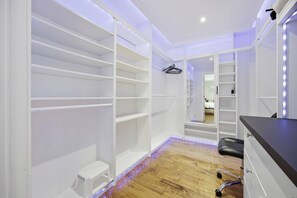 Ein begehbarer Kleiderschrank mit offenen Regalen, einem kleinen Hocker und einem Spiegel.