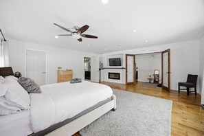 A modern bedroom with a large bed, a ceiling fan, a fireplace, and a TV mounted on the wall. - Bayside Serenity | Parking | Midland Cottage (Midland)