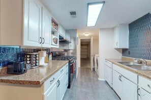 A kitchen with white cabinets, a microwave, a gas stove, a toaster, and a sink.