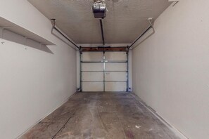 A garage with a closed garage door, concrete floor, and a ceiling-mounted electrical box.