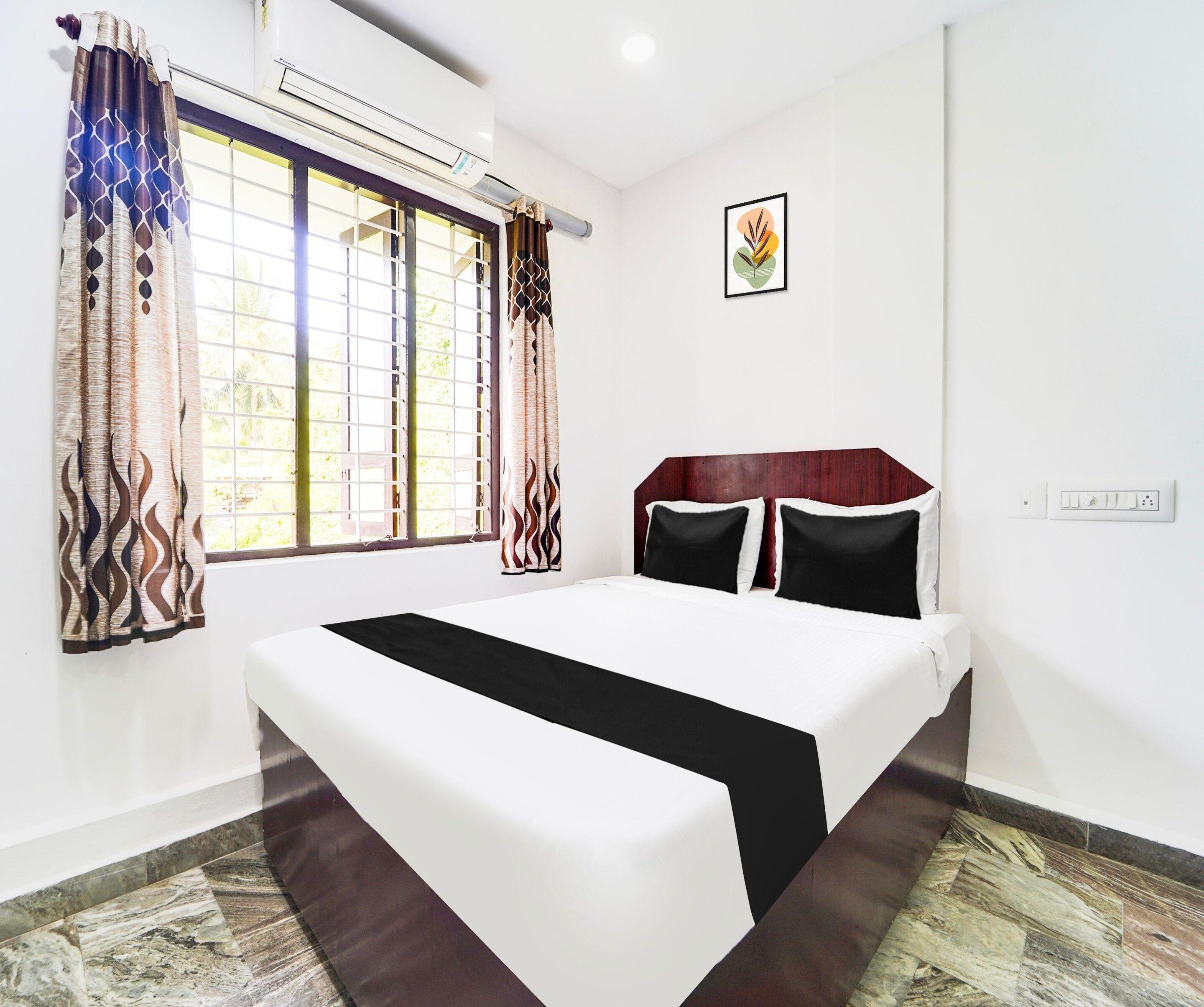 Habitación de hotel con cama, cortinas, ventana, un cuadro en la pared y un enchufe.