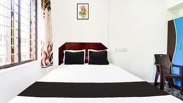 A hotel room with a bed, a desk, a chair, a window with a view, and a wall-mounted picture.
