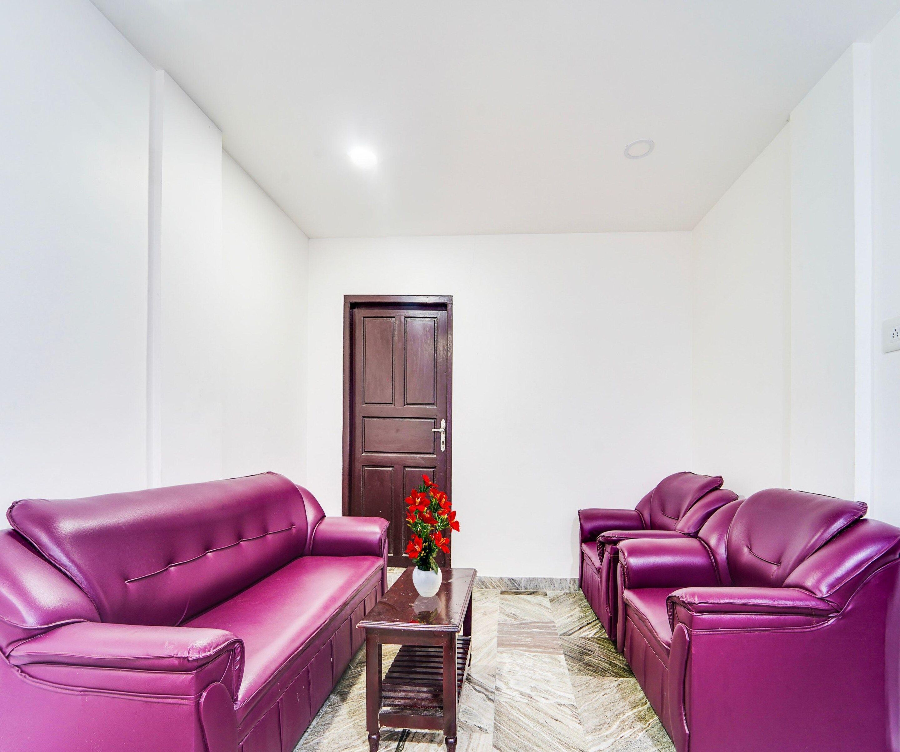 A room with a dark wooden door, a small table with a vase of red flowers, and two purple leather sofas.