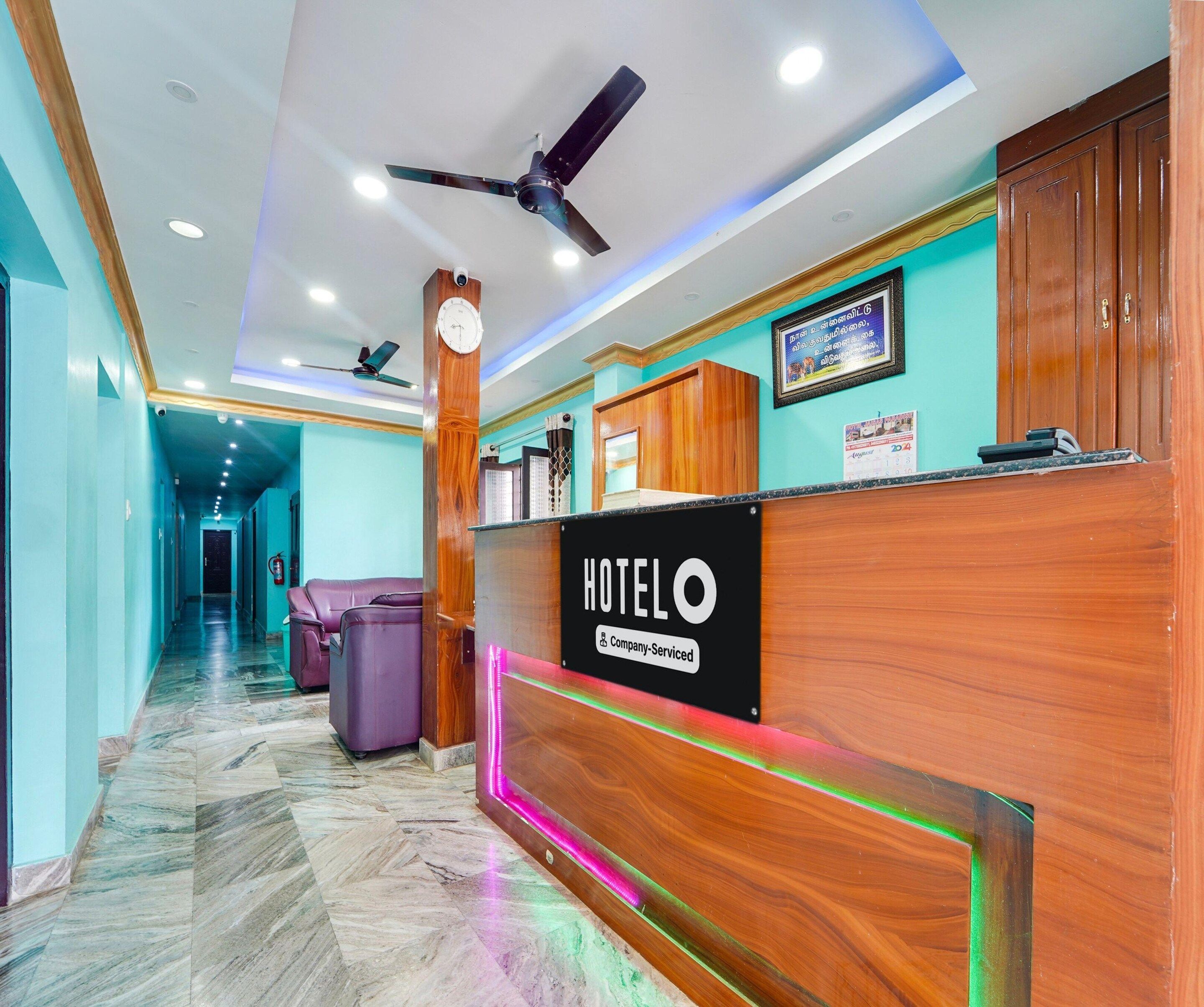 A hotel reception desk with a clock, a ceiling fan, and a sign indicating it is company-serviced.