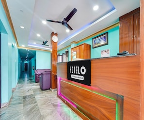 Mostrador de recepción de hotel con un reloj, un ventilador de techo y un cartel que indica servicio de empresa.
