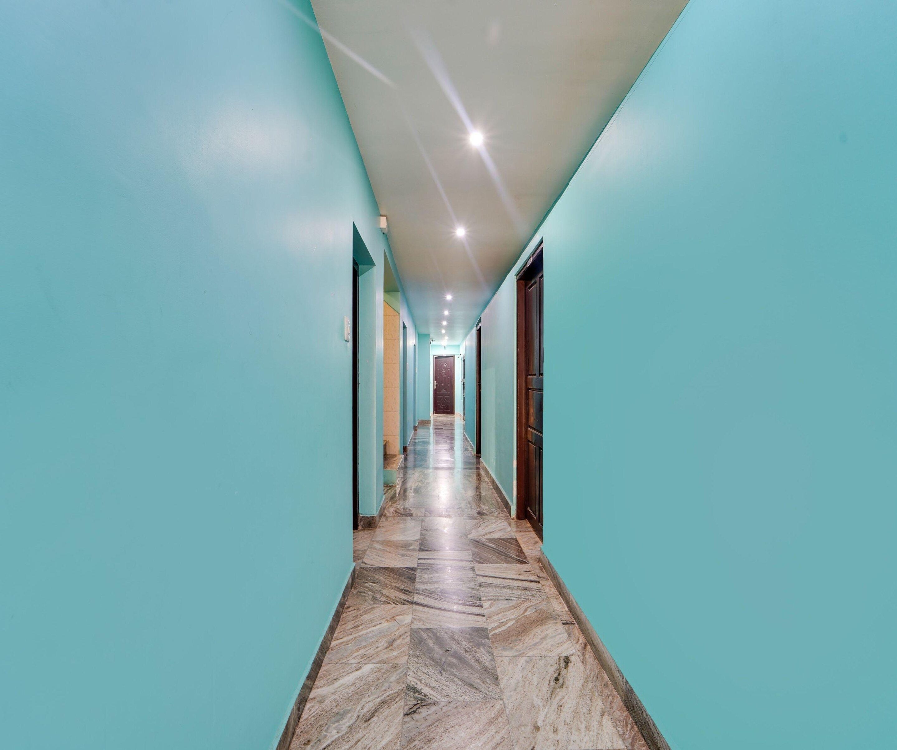 A corridor with teal walls and a marble floor leading to a door at the end.