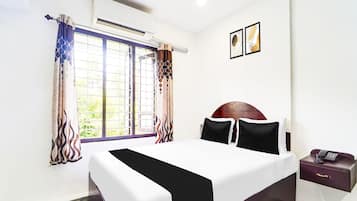 Habitación de hotel con cama, mesita de noche, equipo de aire acondicionado, ventana con cortinas y teléfono instalado en la pared.