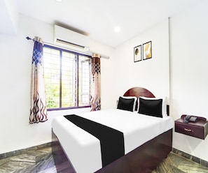 A hotel room with a bed, a nightstand, an air conditioning unit, a window with curtains, and a wall-mounted phone. - Classic Hotel Jaisas Paradise (Nagercoil)