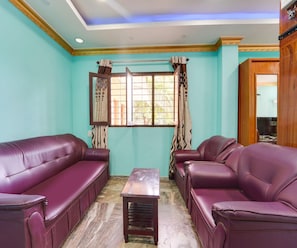 A living room with two purple leather sofas, a wooden coffee table, and a window with curtains. - Classic Hotel Jaisas Paradise (Nagercoil)