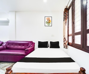 Una habitación con cama, sofá púrpura y ventana con cortinas.