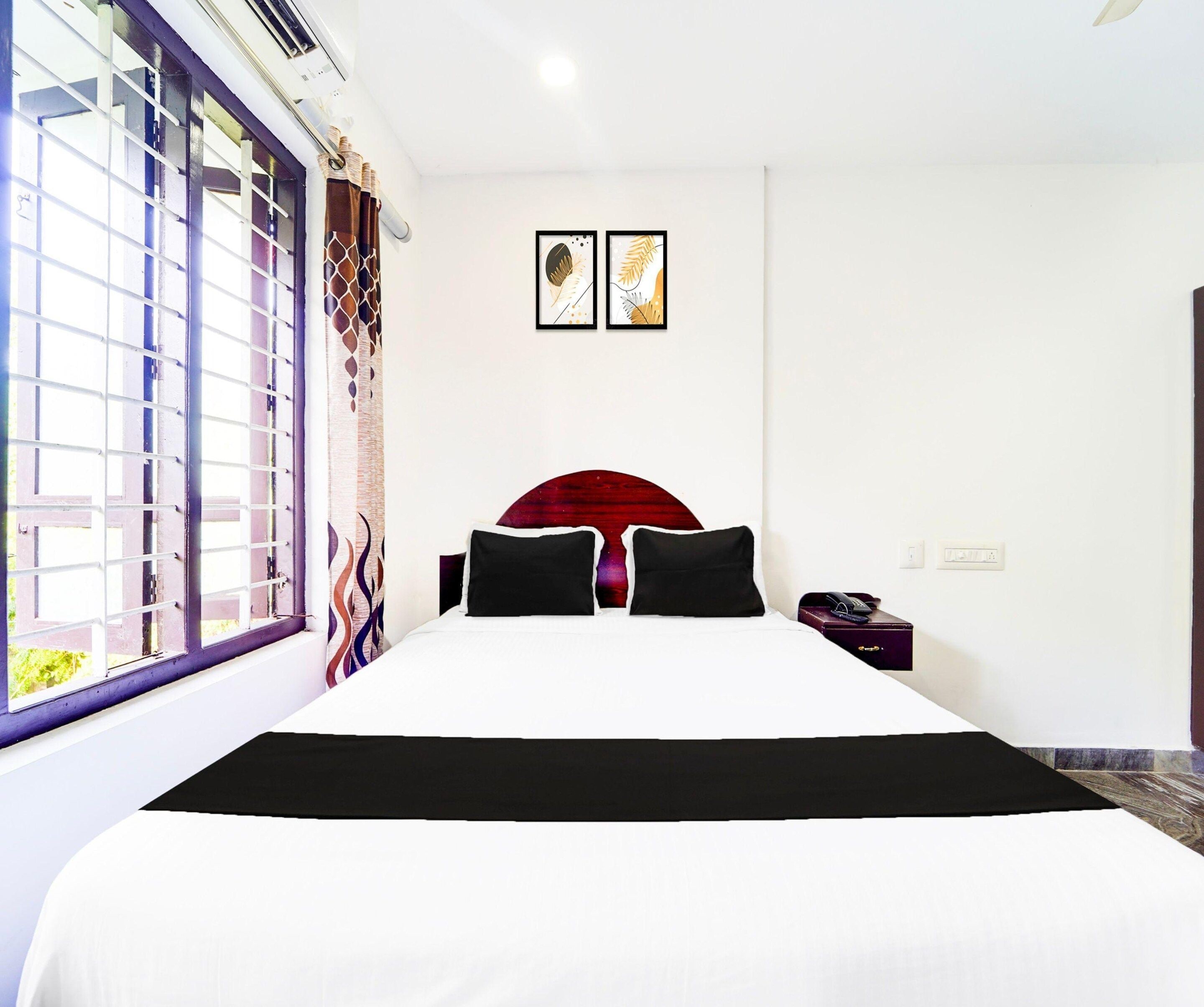 A hotel room with a large bed, a window with bars, a wall-mounted phone, and two framed pictures.