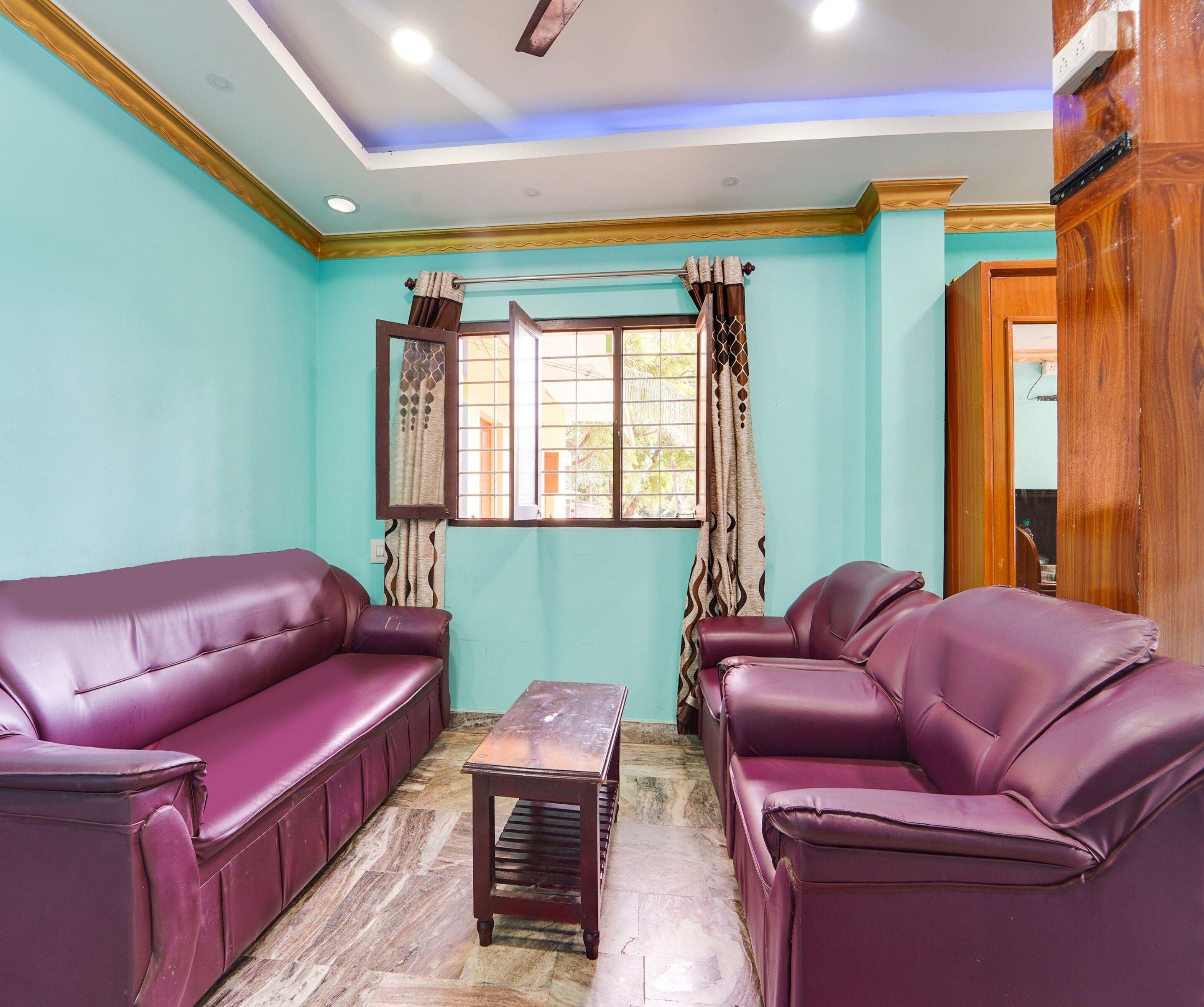 A room with two purple leather sofas, a wooden coffee table, and a window with curtains.