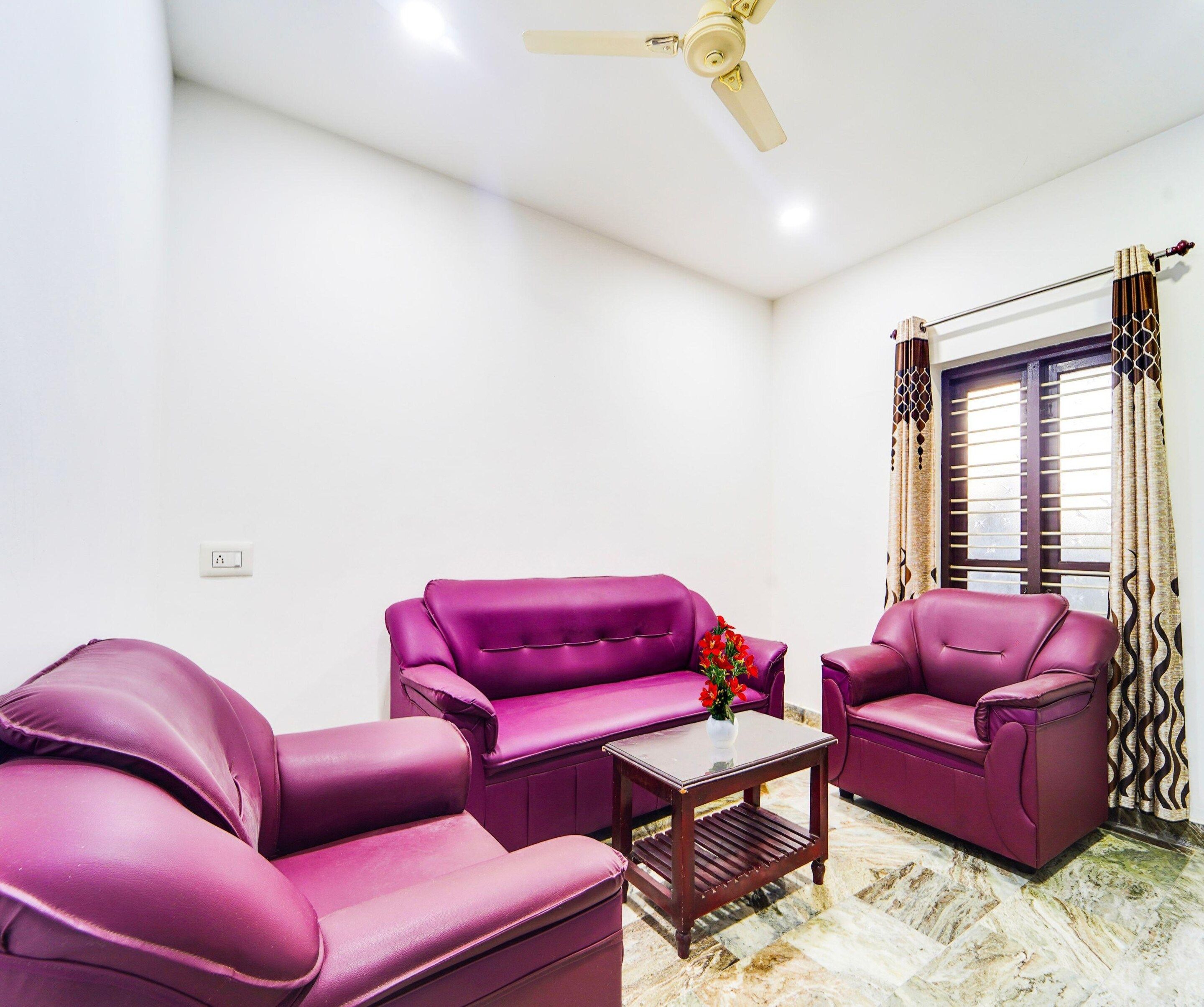 A room with two purple sofas, a small wooden coffee table, and a ceiling fan.