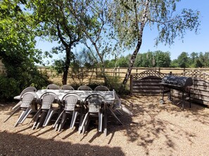 An outdoor dining area with a table and chairs, a grill, and a fence in the background. - Authentic Estate in the Dordogne With a Pool (Saint-Saud-Lacoussiere)