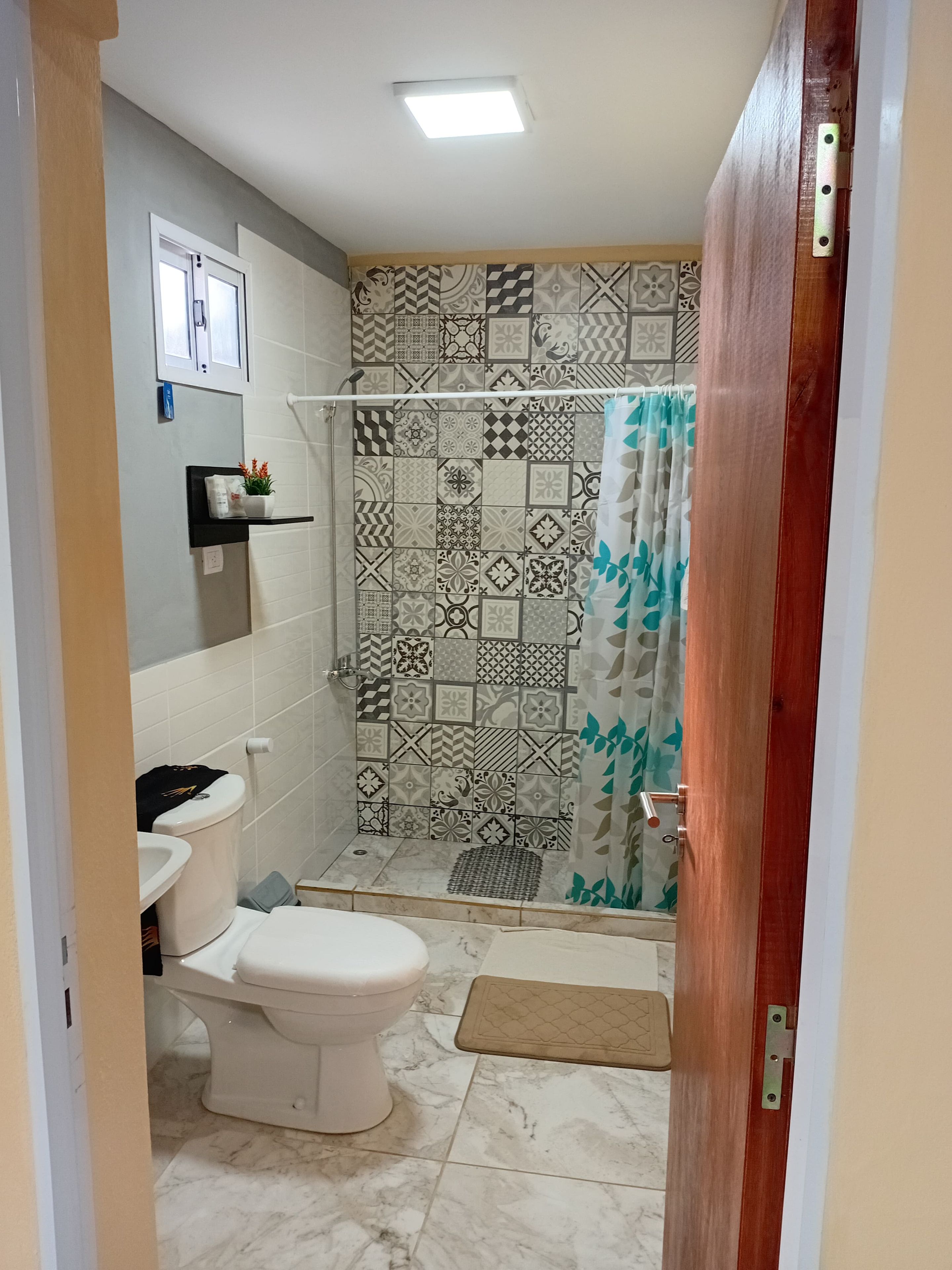 Een badkamer met een toilet, een douche met betegelde wanden en een deur met metalen handgreep.