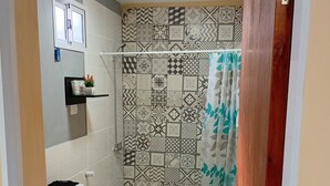 Een badkamer met een toilet, een douche met betegelde wanden en een deur met metalen handgreep.