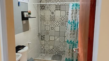 Een badkamer met een toilet, een douche met betegelde wanden en een deur met metalen handgreep.