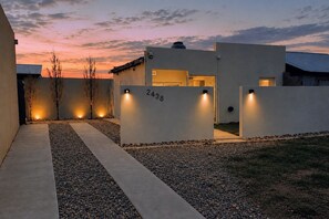 A modern building with a numbered address, outdoor lighting, and a gravel pathway. - GENESIS APARTMENT (Puerto San Julian)