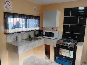 Cozinha compacta com pia, micro-ondas, fogão e armário.