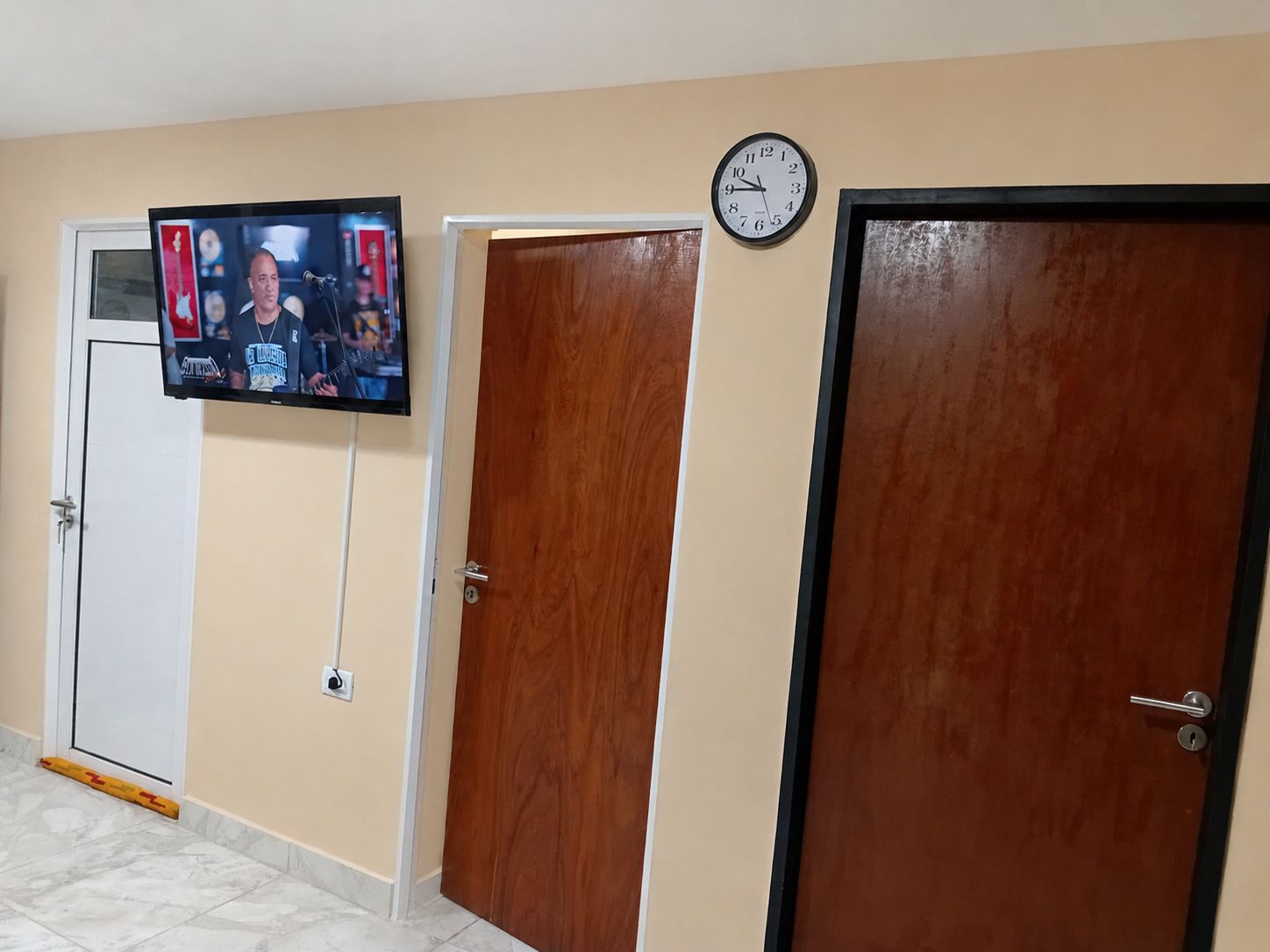 Un pasillo con un televisor montado en la pared, un reloj y tres puertas.