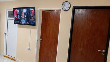 Un pasillo con un televisor montado en la pared, un reloj y tres puertas.