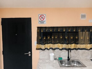 Une cuisine équipée d’un évier, d’une porte et d’un panneau indiquant qu’il est interdit de fumer.