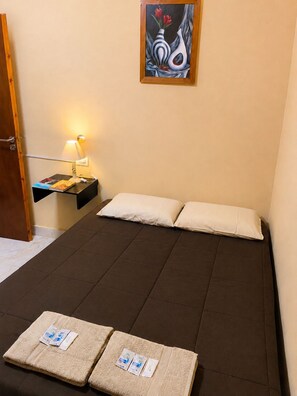A single bed with two pillows and a bedside table with a lamp and a book.