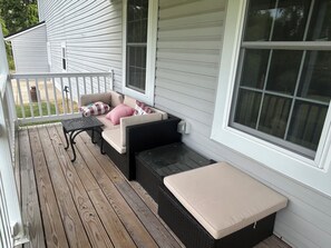 A covered porch with a cushioned seating area, a small table, and a window with blinds. - Private 1-bedroom Highland Cow apartment in Saint Leonard (Saint Leonard)