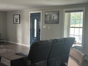 Una habitación con una puerta azul oscuro, un sillón de cuero negro y una ventana que da a vistas de vegetación.