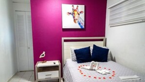 Ein Schlafzimmer mit einem Bett, einem Nachttisch, einem Wandbild und einem Fenster mit Jalousien.