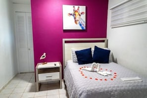 A bedroom with a bed, a nightstand, a wall painting, and a window with blinds. - Cozy 1BR Getaway in Beautiful Aguada,PR AC & Comfort (Aguada)