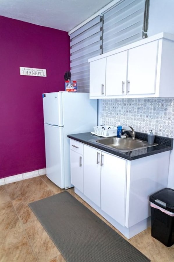 A compact kitchen with white cabinets, a stainless steel sink, and a purple wall. - Cozy 1BR Getaway in Beautiful Aguada,PR AC & Comfort (Aguada)