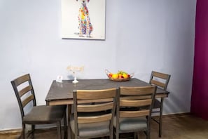 A dining area with a wooden table and chairs, a fruit basket, and a wall-mounted painting. - Cozy 1BR Getaway in Beautiful Aguada,PR AC & Comfort (Aguada)