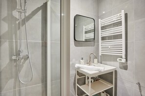 A modern bathroom with a glass-enclosed shower, a white sink with a mirror, and a towel rack. - Elegant Apartment With AC - Center of Paris (Paris)