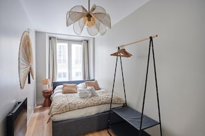 A bedroom with a bed, a hanging light fixture, a window with curtains, and a wall-mounted fan. - Elegant Apartment With AC - Center of Paris (Paris)