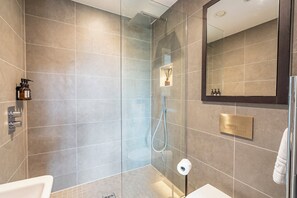 Moderni kylpyhuone, jossa on lasiseinällä varustettu suihku, wc ja pesuallas.