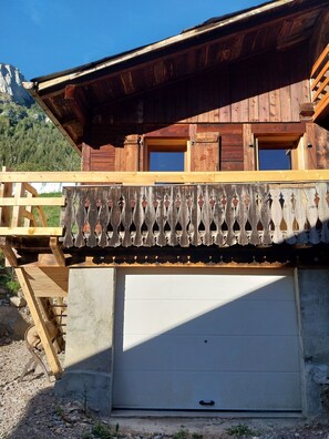A wooden building with a garage door, a wooden balcony with a lattice railing, and a mountain in the background. - Menziesii Vacation Rental. In a traditional farmhouse just 5 minutes from the village center (Abondance)