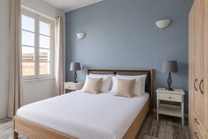 Quarto com uma cama grande, duas mesas de cabeceira, um guarda-roupa e uma janela com cortinas.
