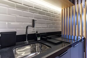 Een moderne keuken met een RVS spoelbak, een zwart aanrecht en een witte betegelde spatwand.
