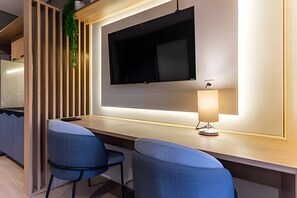 A modern kitchen with a flat-screen TV mounted on the wall, a wooden countertop, and two blue chairs. - Nato Itaim (São Paulo)