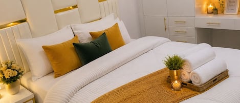 Un dormitorio ordenado con cama, mesitas de noche, un aparador y un estante con toallas y una planta pequeña.