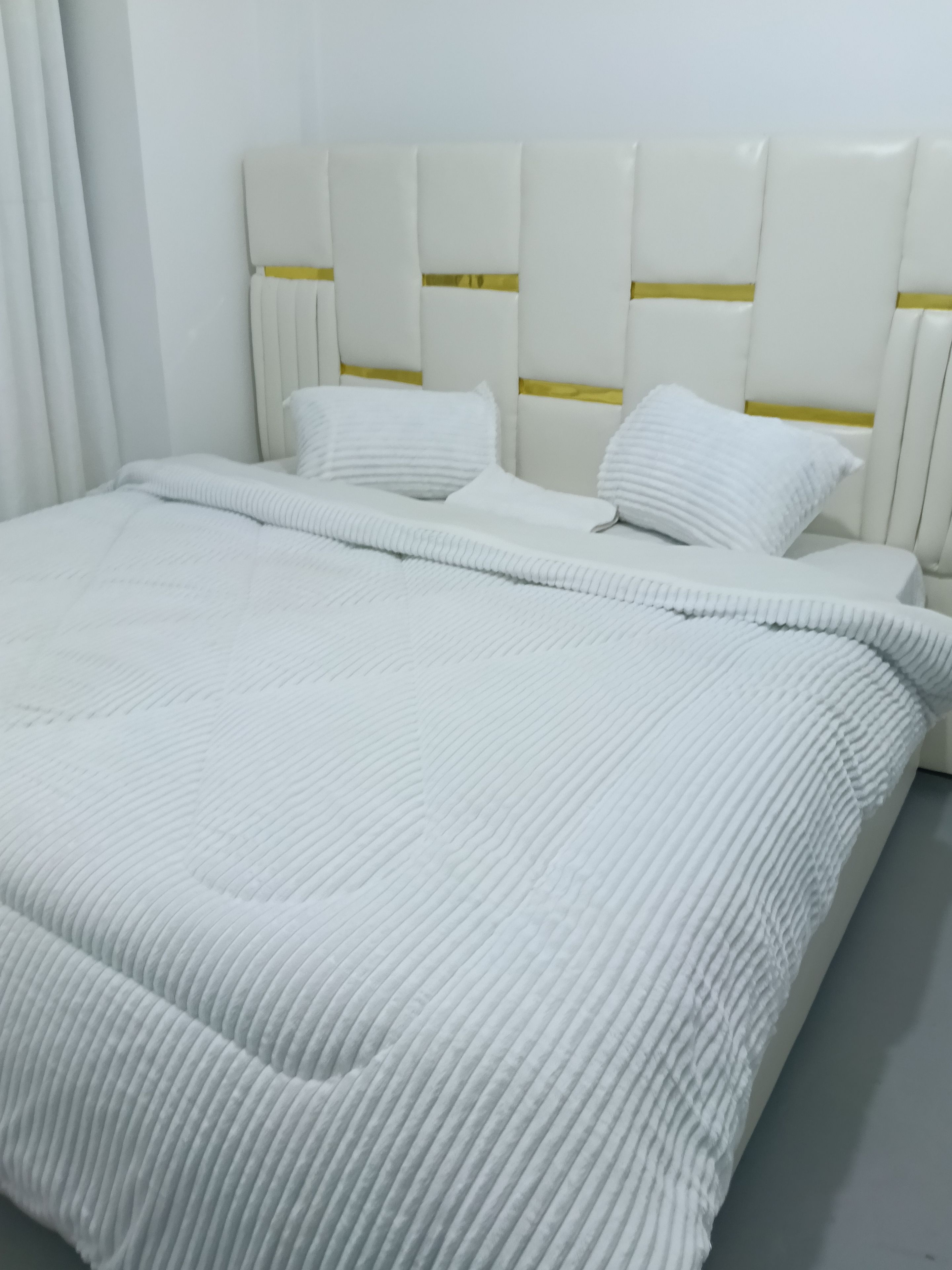 A bed with a white headboard and pillows, a white bedspread, and a white curtain.