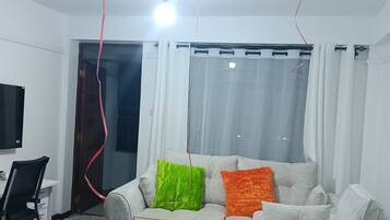 A living room with a grey sofa, colorful cushions, a white coffee table, and three balloons tied to the ceiling.